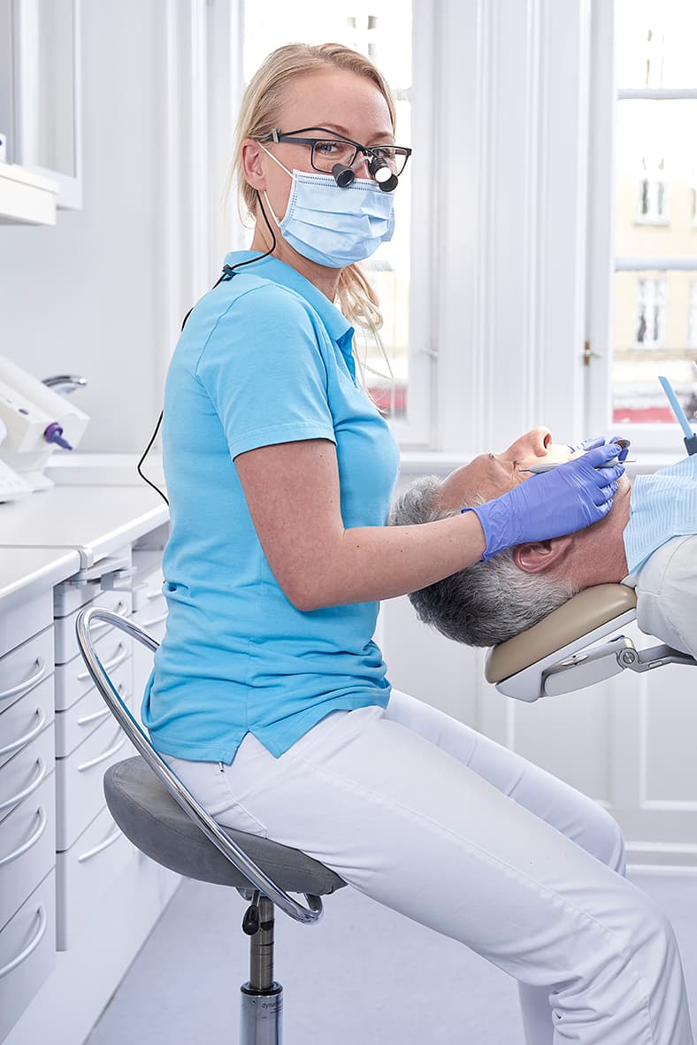 Kvindelig tandlæge sidder på en InCharge stol og arbejder. Patient ligger i patientstol.